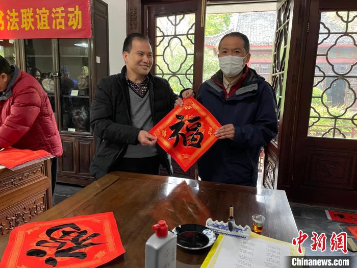 圖為一名日本人(右)展示其書寫的春聯(lián)?！×周?攝