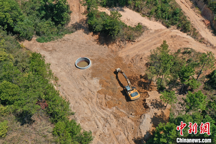 9月6日，在鄱陽湖畔的江西省九江市都昌縣多寶鄉(xiāng)林場，一臺挖掘機不停揮舞著“大臂”，為一口直徑5米、深8.5米的蓄水池進行場地平整，山泉水順著一根水管緩緩注入蓄水池內(nèi)。（無人機照片） <a target='_blank' href='/'>中新社</a>記者 劉占昆 攝