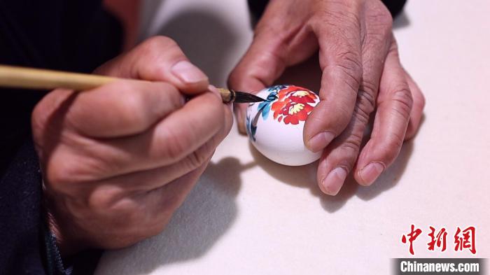 高觀凌一手拿蛋殼，一手持繪筆。片刻間，一朵美麗的牡丹花便“綻放”于蛋殼之上?！￡皷|明 攝